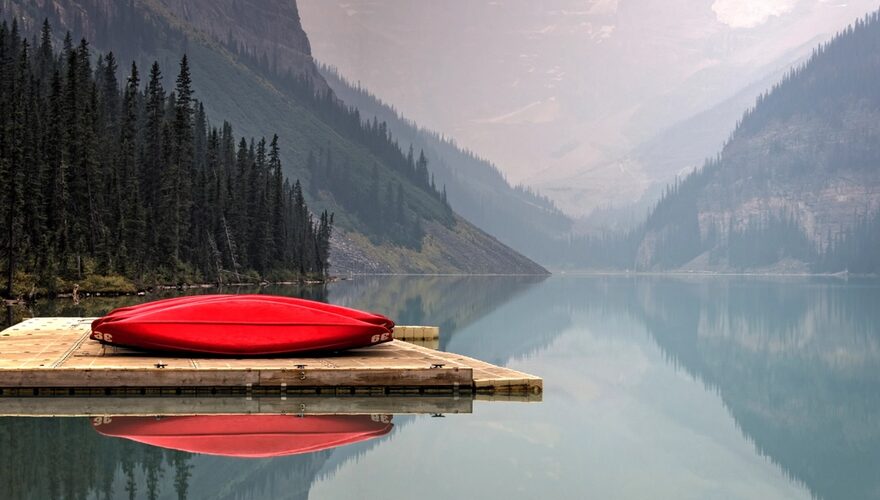 A red canoe on a wooden dock on a still turquoise lake in the Canadian Rockies