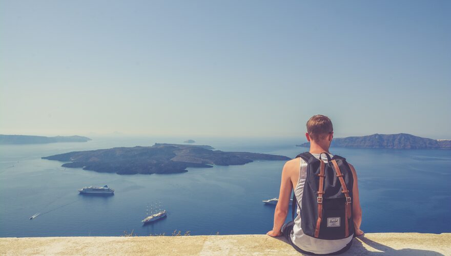A traveller with a backpack looking out over the Aegean caldera from Oia, Santorini